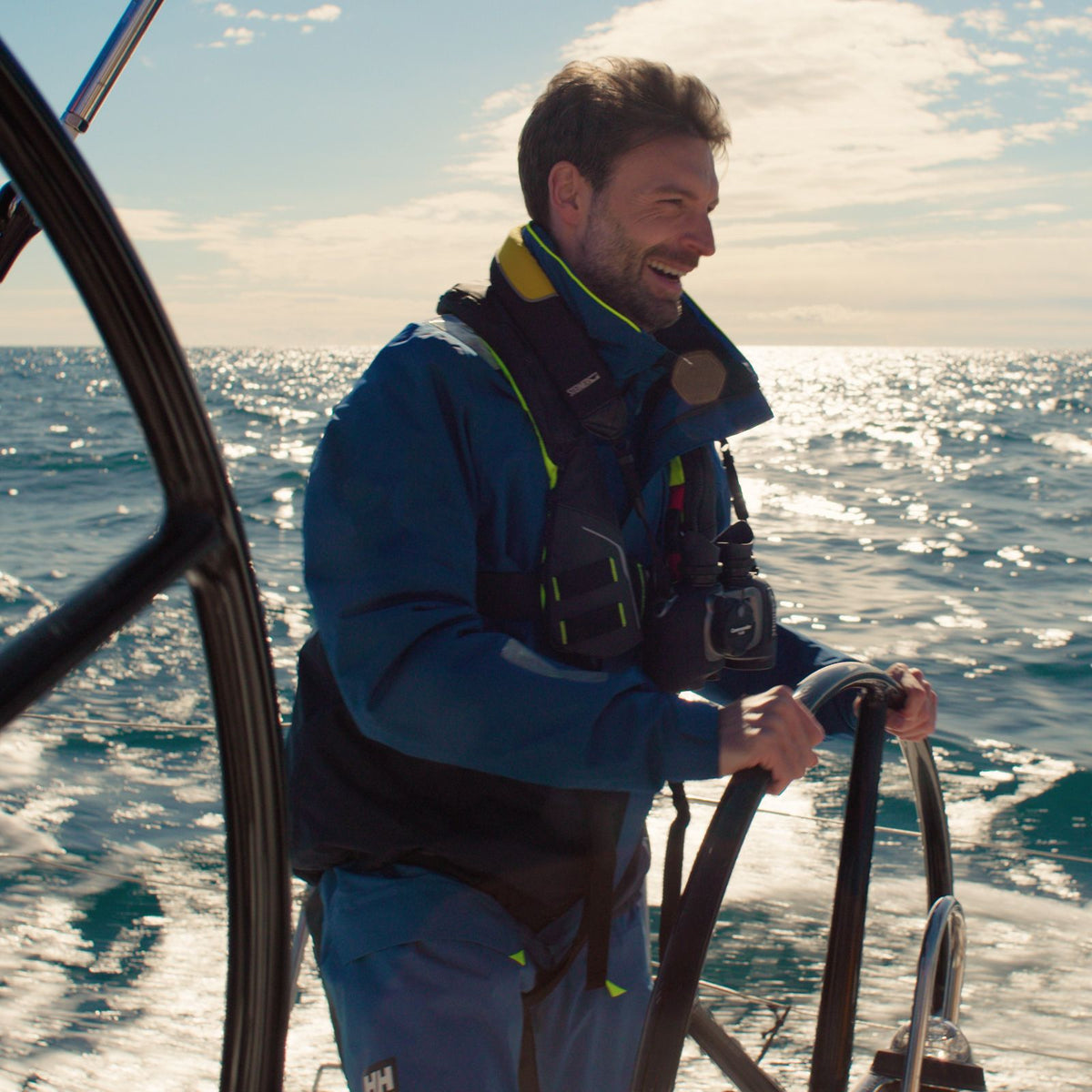 Steiner Schwimmtragegurt für Commander 7x50 – Segler am Steuerrad eines Segelboots auf offener See, STEINER Fernglas am Hals, Helly-Hansen-Ausrüstung