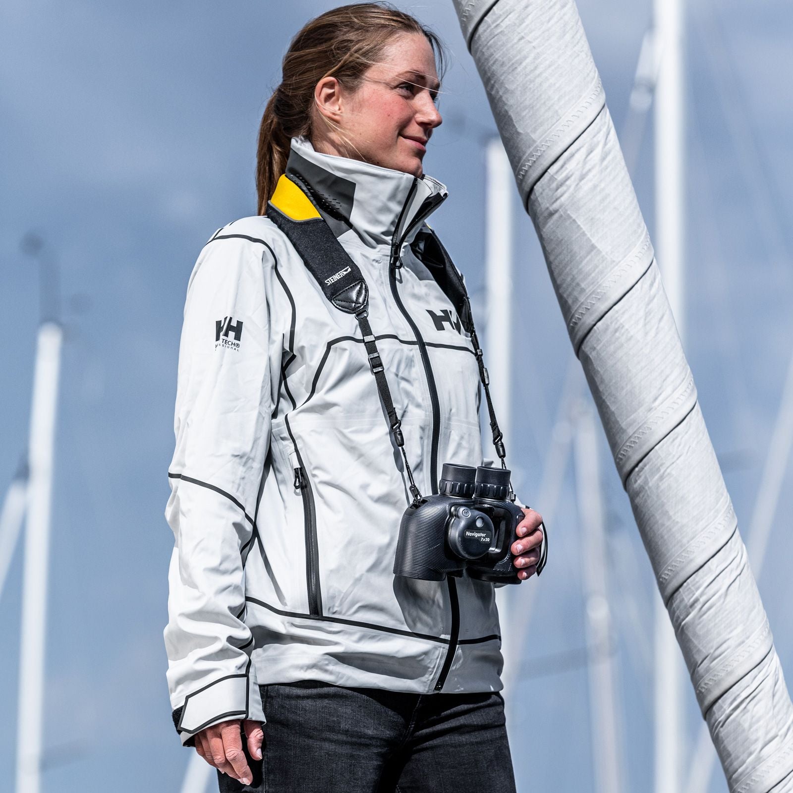 Steiner Schwimmtragegurt für Navigator – Seglerin mit STEINER Navigator-Fernglas am Segelmast in weißer Helly-Hansen-Jacke