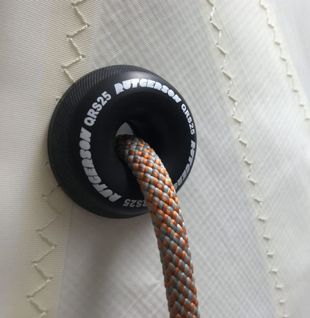 RUTGERSON Quick Reef Ring QRS25 am weißen Segeltuch montiert, mit weißem Markenaufdruck und einer grau-orange geflochtenen Reffleine durch die zentrale Öffnung.